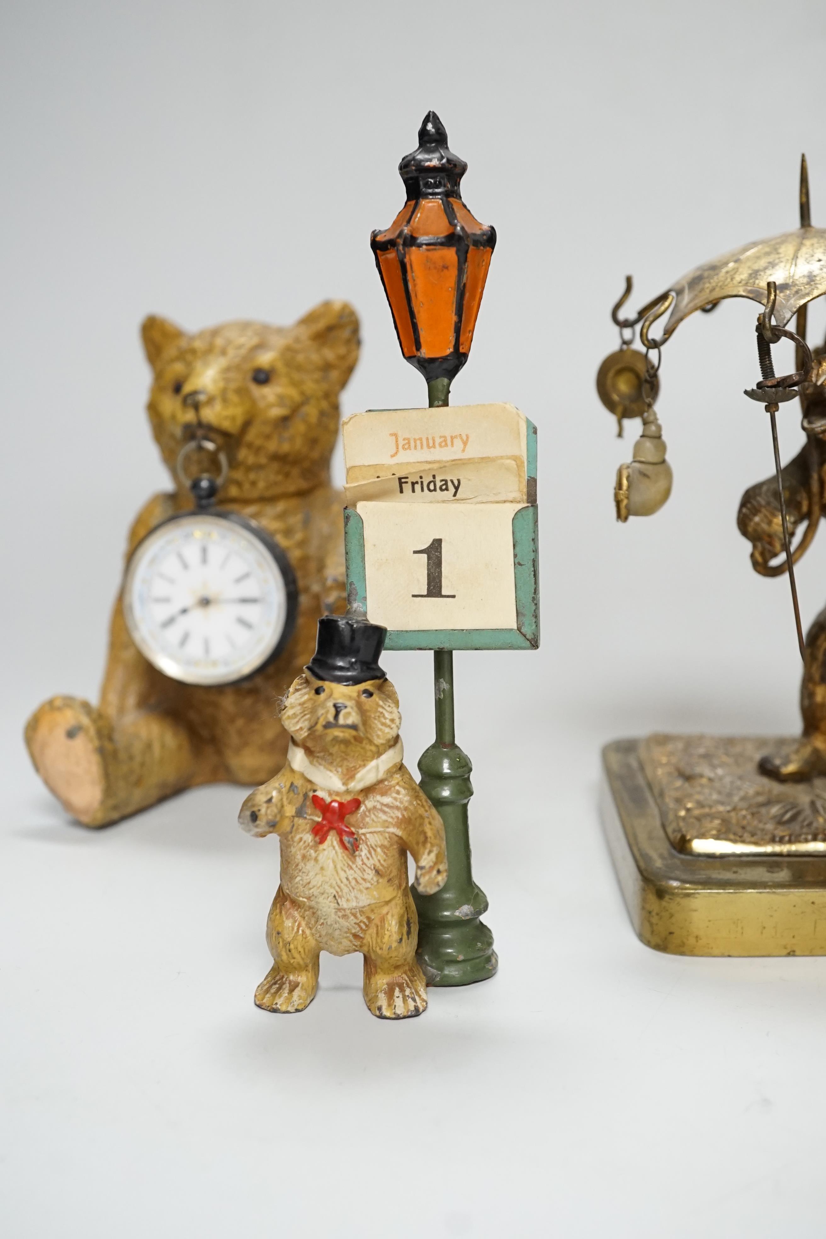 A Smith teddy bear clock, a seated metal bear holding a pocket watch, a metal standing bear with parasol and a German metal bear calendar